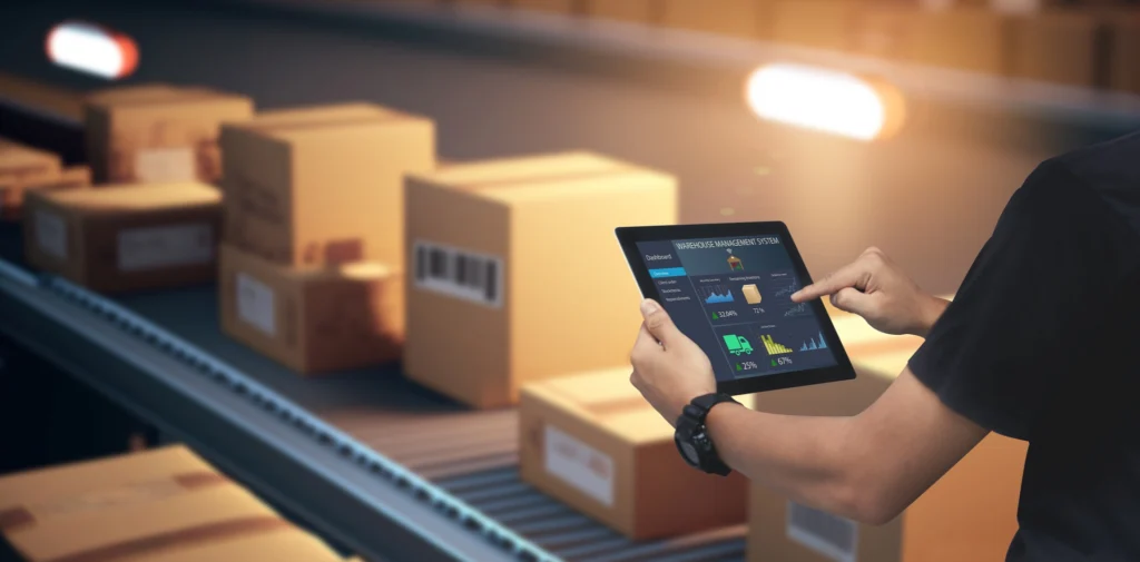 Warehouse worker using a tablet next to a conveyor belt moving packages